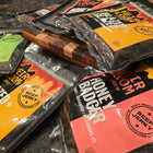 Numerous bags of all three flavors of beef jerky on a counter top with a cutting board.