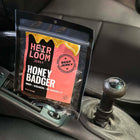 A bag of Honey Badger beef jerky by Heirloom Jerky sitting in the center console of a car just behind the stick shift.