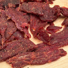 A closeup photo of Sauce Slinger beef jerky that shows the seasoning and marinade that coats the pieces of jerky.